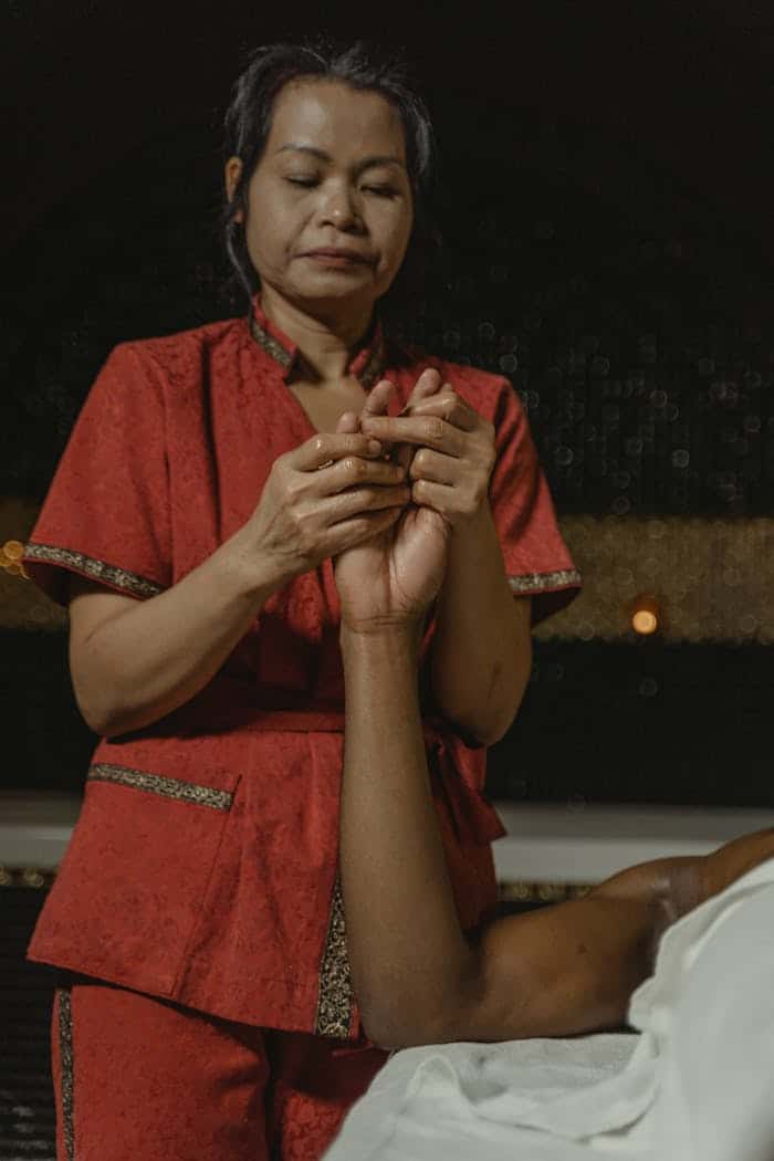 An Asian masseuse giving a hand massage to a client in a serene spa setting.